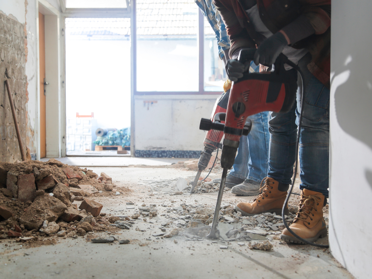 Person, die mit einem Schlaghammer den Betonboden entfernt