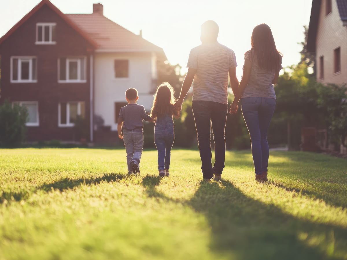 Familie läuft im Garten händehaltend auf Haus zu
